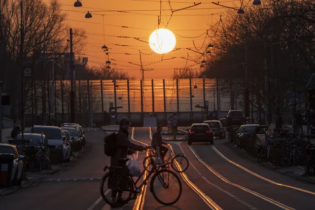 Bicyclists cross tram tracks as evening traffic moves under a setting sun in the Dutch capital of Amsterdam, Netherlands, Wednesday, March 23, 2022. (Photo by Peter Dejong/AP Photo)