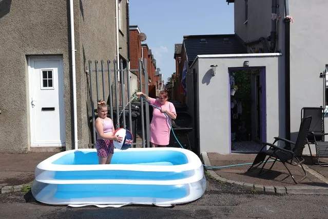 Danielle Lofthouse cools down her daughter Amelia Bradford, 10, with a hose as they enjoy the hot weather off the Shankill Road in north Belfast on July 18, 2022. (Photo by Liam McBurney/PA Images via Getty Images)