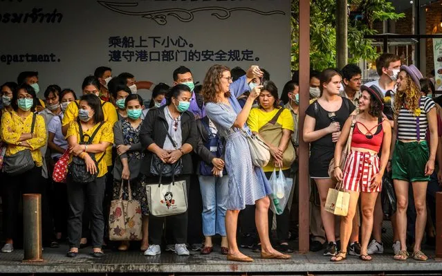 Tourists take pictures next to commuters with facemasks, worn amid fears of the spread of the COVID-19 novel coronavirus, as they wait for a canal boat in Bangkok on March 2, 2020. A Thai man has died from complications doctors say were due to the deadly coronavirus, though health officials were reluctant on March 2 to conclusively confirm the cause of his death. (Photo by Mladen Antonov/AFP Photo)