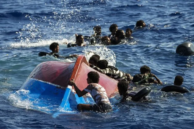 Migrants swim next to their overturned wooden boat during a rescue operation by Spanish NGO Open Arms at south of the Italian Lampedusa island at the Mediterranean sea, Thursday, August 11, 2022. Forty migrants from Eritrea and Sudan, two children and one woman, were rescued by NGO Open Arms crew members and Italian coast guard after their boat overturned and started to sink. (Photo by Francisco Seco/AP Photo)