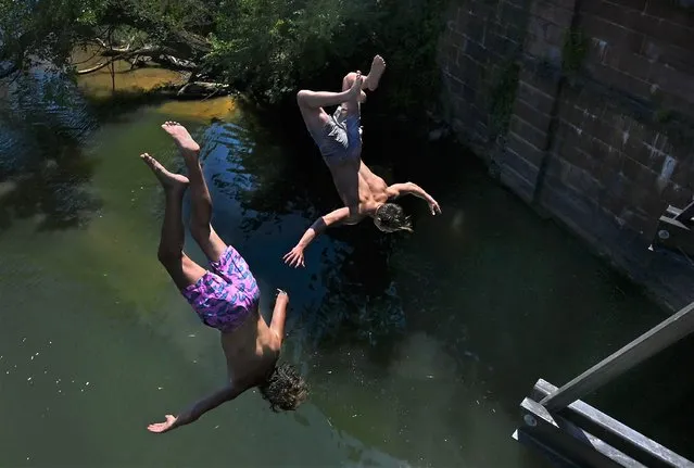 (L) Trey Cook and Charlie Thomas (both are from Darnestown, Maryland) look like synchronized divers as they made the leap from the C & O canal foot bridge at Riley's Lock into Seneca Creek at the mouth of the Potomac River in Poolesville, Maryland on July 23, 2022. The Potomac River was a popular destination this weekend for locals trying to beat the heat. Temperatures reached the high 90's today in Montgomery County. (Photo by Michael S. Williamson/The Washington Post)