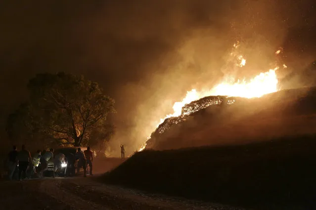 People push a van that got stuck bringing water for volunteers to fight a wild fire raging near houses in the outskirts of Obidos, Portugal, in the early hours of Monday, October 16 2017. Wildfires in Portugal killed at least 27 people, injured dozens more and left an unconfirmed number of missing in the country's second such tragedy in four months, officials said Monday. (Photo by Armando Franca/AP Photo)
