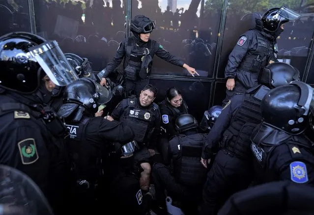 A couple of police officers lean against a protection barrier in pain surrounded by fellow officers, after being injured by an explosive device thrown by protesters during clashes outside of Mexico's Attorney General's Office in Mexico City, Thursday, September 22, 2022. The demonstrators were marching ahead of the anniversary of the 2014 disappearance of 43 students of a teachers’ college in Iguala, Guerrero. Multiple police were injured by the explosion and loaded onto ambulances. (Photo by Fernando Llano/AP Photo)