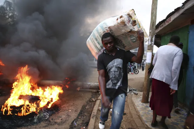 A Kenyan carries his belongings as he passes a fire lit by National Super Alliance (NASA) supporters in Nairobi's Kibera slums, after burning tyres to block the roads Wednesday October 25, 2017, a day before the country goes to the polls, calling for a boycott of the elections. The chief justice of Kenya's Supreme Court says the court cannot hear a last-minute petition to postpone Thursday's presidential election because it does not have a quorum of judges. Chief Justice David Maraga appeared alone in the court Wednesday morning and said only he and one other judge had been able to attend the hearing. The announcement appears to open the way to Thursday's vote proceeding. (Photo by AP Photo/Stringer)