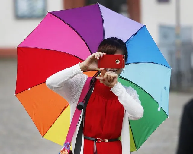 A Chinese tourist with a colorful umbrella takes a picture visiting the Roemerberg square in Frankfurt, Germany, on a warm Friday, July 29, 2016. (Photo by Michael Probst/AP Photo)