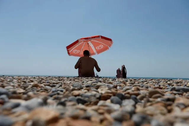 A man sits under an umbrella on Brighton beach, during a heatwave in Brighton, Britain, July 19, 2022. (Photo by Peter Cziborra/Reuters)
