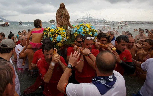 Divers and fishermen carry the image of the Virgin of Palm as a girl touch it at El Rinconcillo beach during the yearly Virgin of Palm maritime pilgrimage on August 15, 2016 in Algeciras, Spain. The Our Lady of Palm maritime pilgrimage in Algeciras dates back to 1975 and takes place annually when fishermen rescue the submerged virgin from the deep sea. Worshippers amid thousands of visitors await its arrival at the Rinconcillo beach. The devotion for the Virgin of Palm comes from the seventeenth century when a ship coming from Italy docked at Algeciras port to wait out bad weather. According to legend, once the crew of the ship removed a box with an image of the Virgin from its cargo the weather turned and the sea's tides were calmed. (Photo by Pablo Blazquez Dominguez/Getty Images)