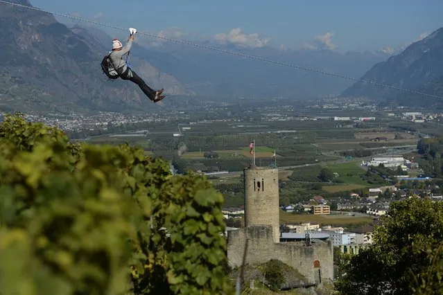 A man slips down the zipline before the opening of the fair “Foire du Valais” above the town of Martigny, Switzerland, 02 October 2014. The Zipline is made of 1'123 meters of cable; it takes one minute 10 to slip down, passes an altitude of 120 meters and a speeds of up to 85 km. According the organizer of the fair the Zipline driving through a town of 18,000 inhabitants, should be unique in the world. (Photo by Maxime Schmid/EPA)