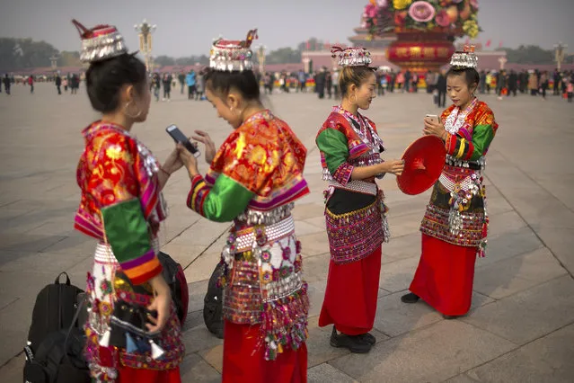 Women in ethnic minority dress look at their smartphones as they stand on Tiananmen Square in Beijing, Monday, November 6, 2017. U.S. President Donald Trump will visit China's capital on a on a three-day state visit beginning on Wednesday. (Photo by Mark Schiefelbein/AP Photo)
