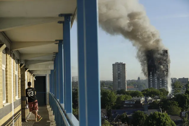 A resident in a nearby building watches smoke rise from the Grenfell Tower on fire in London on June 14, 2017. A massive fire raced through the high-rise apartment building in west London, killing at least 80 people and injuring many others. (Photo by Matt Dunham/AP Photo)