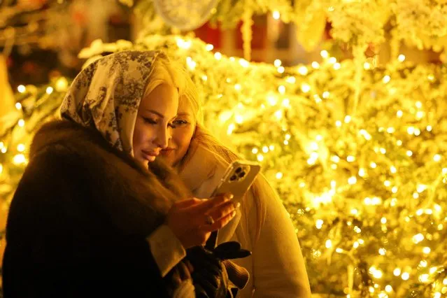 Women look at a mobile phone at a Christmas market on Manezh Square in Moscow, Russia on December 26, 2022. (Photo by Evgenia Novozhenina/Reuters)