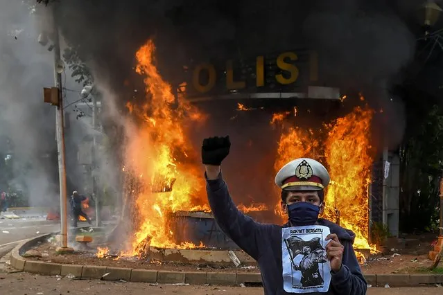 A demonstrator stands for pictures in front of a burning police station in Jakarta, Indonesia, October 8, 2020. The “omnibus” jobs creation bill, passed into law on Monday, has seen thousands of people in Southeast Asia’s largest economy take to the streets in protest against legislation they say undermines labour rights and weakens environmental protections. (Photo by Galih Pradipta/Antara Foto via Reuters)