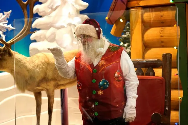 Santa Claus waves at children and their families from behind a transparent barrier at Bass Pro Shops, Friday, November 20, 2020, in Miami. This is Santa Claus in the Coronavirus Age, where visits are done with layers of protection or moved online. Putting hundreds of kids a day onto your lap to talk directly into your face — that's not happening. (Photo by Lynne Sladky/AP Photo)