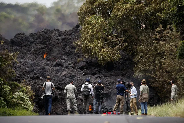 Members of the media record a wall of lava entering the ocean near Pahoa, Hawaii, Sunday, May 20, 2018. Kilauea volcano, oozing, spewing and exploding on Hawaii's Big Island, has gotten more hazardous in recent days, with rivers of molten rock pouring into the ocean and flying lava causing the first major injury. (Photo by Jae C. Hong/AP Photo)