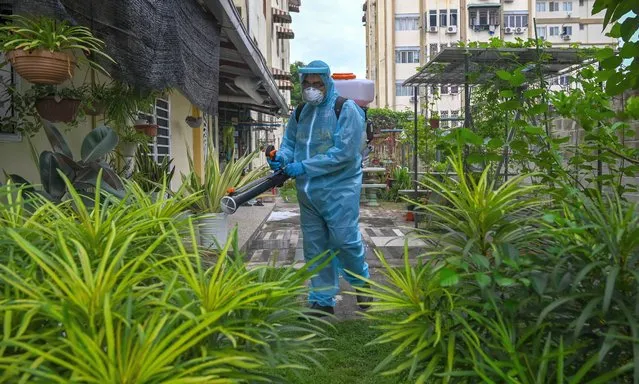 A city council volunteer worker wearing protective gear sprays disinfectant, amid the COVID-19 coronavirus pandemic, in the backyard of an apartment building in Kuala Lumpur on October 26, 2020. (Photo by Mohd Rasfan/AFP Photo)