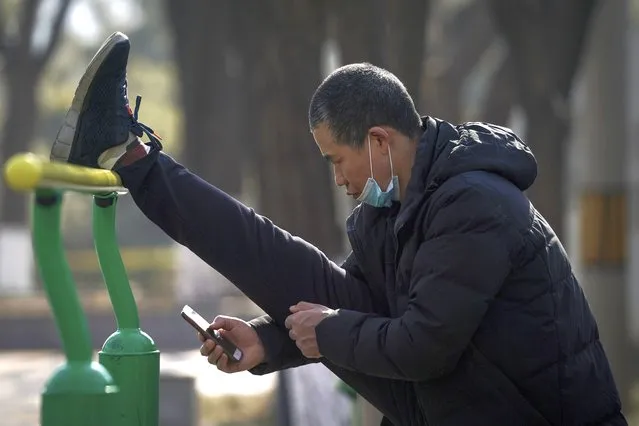 A man wearing a face mask to help curb the spread of the coronavirus browses his smartphone while stretching his leg at a public park in Beijing, Tuesday, January 26, 2021. Countries must cooperate more closely in fighting the challenges of the pandemic and climate change and in supporting a sustainable global economic recovery, Chinese President Xi Jinping said on Monday in an address to the World Economic Forum. (Photo by Andy Wong/AP Photo)