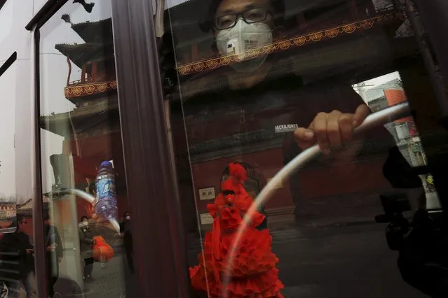A man wearing a protective mask looks from inside a bus as Chinese artist Kong Ning walks in her costume made of hundreds of orange plastic blowing horns during her art performance raising awareness of the hazardous smog in a historical part of Beijing on a very polluted day December 7, 2015. (Photo by Damir Sagolj/Reuters)