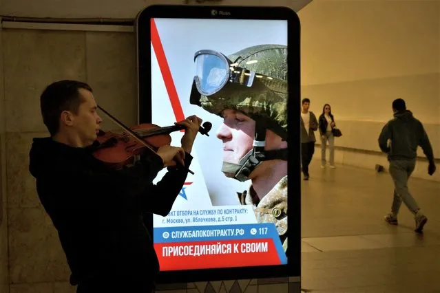 A street musician plays his violin by an advertising screen promoting contract military service in the Russian army at the Moscow metro on June 2, 2023. (Photo by Natalia Kolesnikova/AFP Photo)