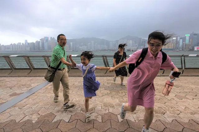 Mainland Chinese tourists run along a promenade during a typhoon in Hong Kong, Monday, July 17, 2023. Schools and the stock market were closed in Hong Kong on Monday as Typhoon Talim swept south of the city. (Photo by Louise Delmotte/AP Photo)