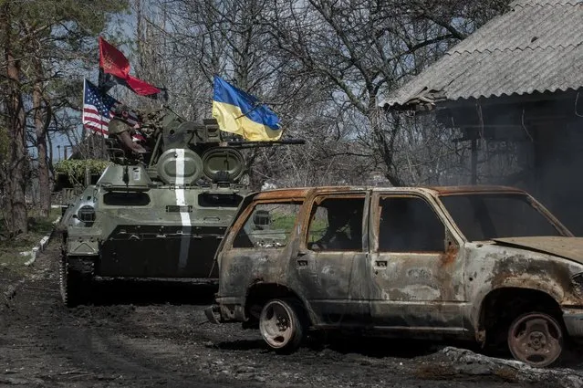 Ukrainian servicemen ride in an armored vehicle, with Ukrainian and US flags and nationalist group Right Sector flag, near a destroyed car in Shyrokyne, eastern Ukraine, Wednesday, April 15, 2015.  Russia and Ukraine agreed in Berlin on Monday to call for the pullback of smaller-caliber weapons from the front lines of the conflict that has claimed more than 6,000 lives. (AP Photo/Evgeniy Maloletka)