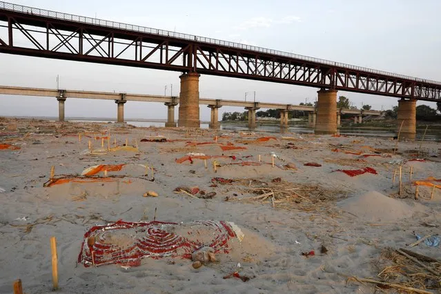 Bodies of suspected coronavirus victims are seen in shallow graves buried in the sand near a cremation ground on the banks of Ganges River in Prayagraj, India, Saturday, May 15, 2021. Police are reaching out to villagers in northern India to investigate the recovery of bodies buried in shallow sand graves or washing up on the Ganges River banks, prompting speculation on social media that they were the remains of COVID-19 victims. (Photo by Rajesh Kumar Singh/AP Photo)