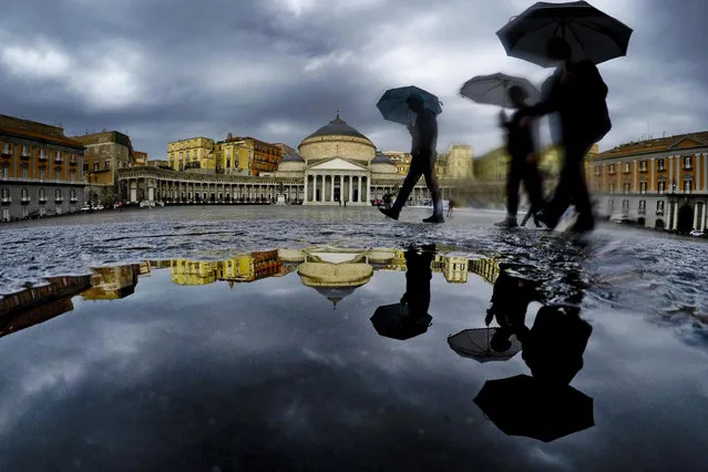 Pedestrians are reflected in a puddle as they protect themselves from the pouring rain with umbrellas while walking in downtown Naples, southern Italy, 22 October 2018. Heavy rains had battered Italy from north to south on 21 October evening with even hailstorms been reported in Rome. Seen in background is the neo-classical Royal Palace at the Piazza del Plebiscito. (Photo by Ciro Fusco/EPA/EFE)