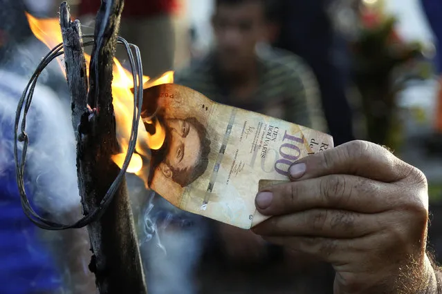 A man burns a 100-bolivar bill during a protest in El Pinal, Venezuela December 16, 2016. (Photo by Carlos Eduardo Ramirez/Reuters)