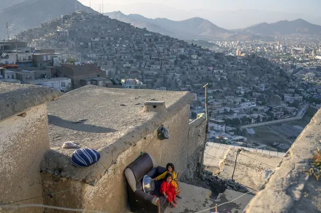 Girls sit on a couch from a home in a hill overlooking Kabul on October 14, 2021. (Photo by Bulent Kilic/AFP Photo)