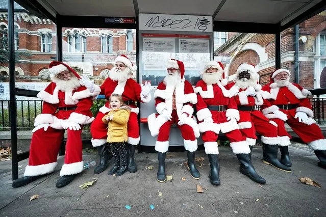 Young passer-by Darcie O'Rourke, 4, is greeted by student santas and an elf waiting at a bus stop as the annual Santa school returns for in person training at the Ministry of Fun's Santa School in London on Tuesday, November 30, 2021. (Photo by Yui Mok/PA Images via Getty Images)