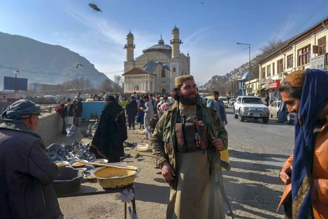 A member of the Taliban stands next to an Afghan hawker selling bird feed at a market area in Kabul on December 3, 2021. (Photo by Ahmad Sahel Arman/AFP Photo)
