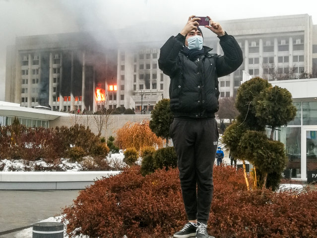 A man takes a picture by the burning mayor’s office in Almaty, Kazakhstan on January 5, 2022. Protests are spreading across Kazakhstan over the rising fuel prices; protesters broke into the Almaty mayor’s office and set it on fire. (Photo by Yerlan Dzhumayev/TASS)