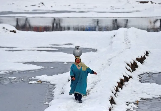 A woman carrying a water pitcher walks through a snow-covered field on the outskirts of Srinagar January 9, 2022. (Photo by Danish Ismail/Reuters)