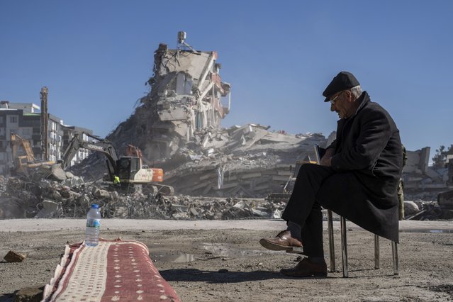 Mehmet Nasir Duran, 67, sits on a chair, as heavy machines remove debris from a building, where five of his family members are trapped in Nurdagi, southeastern Turkey, Thursday, February 9, 2023.Thousands who lost their homes in a catastrophic earthquake huddled around campfires and clamored for food and water in the bitter cold, three days after the temblor and series of aftershocks hit Turkey and Syria. (Photo by Petros Giannakouris/AP Photo)