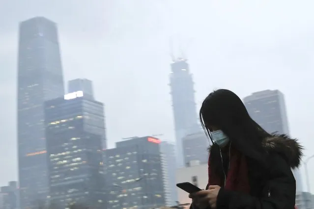 In this February 21, 2017 photo, a woman wearing a mask walks to a subway station during the evening rush hour in Beijing. Yet the city’s average reading of the tiny particulate matter PM2.5 – considered a good gauge of air pollution – is still seven times what the World Health Organization considers safe. A group of Chinese lawyers is suing the governments of Beijing and its surrounding areas for not doing enough to get rid of the smog. (Photo by Andy Wong/AP Photo)