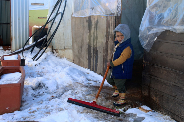 A Syrian boy clears snow from the entrance of a tent in the Syrian refugees camp of al-Hilal in the village of al-Taybeh near Baalbek in Lebanon's Bekaa valley on January 20, 2022. (Photo by AFP Photo/Stringer Network)