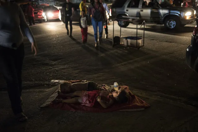 Children sleep in the street near their mother's food stand where she sells food to people attending an event marking the feast day of Our Lady of Chiquinquirá, better know as “Chinita”, in downtown Maracaibo, Venezuela, November 17, 2019. For many in Maracaibo, Venezuela's economic crash in the last five years hit especially hard. Once a center of the nation's vast oil wealth, production under two decades of socialist rule has plummeted to a fraction of its high, taking down residents' standard of living. (Photo by Rodrigo Abd/AP Photo)