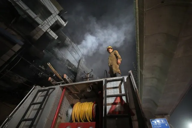 A fire official stands on a fire brigade truck to help his colleagues douse a fire in a four storied building, in New Delhi, India, Saturday, May 14, 2022. A massive fire erupted in a four-storied building in the Indian capital on Friday, killing at least 19 people and leaving several injured, the fire control room said. Dozens of people have been rescued from the commercial building, mainly shops, in the Mundka area in the western part of New Delhi. (Photo by Manish Swarup/AP Photo)