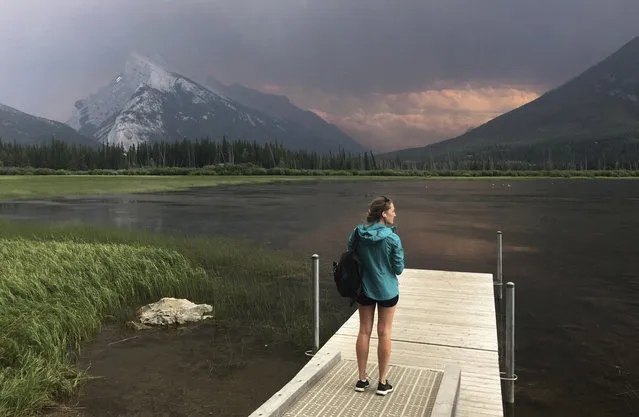 A woman stands on a dock on the Vermillion Lakes near Banff, Alberta, Sunday, July 16, 2017, overlooking Mt. Rundle covered by smoke that came from a wildfire in Kootenay National Park in British Columbia. (Photo by Adrian Wyld/The Canadian Press via AP Photo)