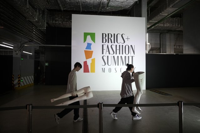 Assistants carry mannequin parts past a poster with an emblem of BRICS+ Fashion Summit in a Parking Gallery at Zaryadye Park near the Kremlin in Moscow, Russia, on Tuesday, November 29, 2023. An international fashion forum in Moscow has brought together designers from Brazil, China, India, South Africa and other countries, an event that underlined Russia's shift away from the West amid the fighting in Ukraine. (Photo by Alexander Zemlianichenko/AP Photo)