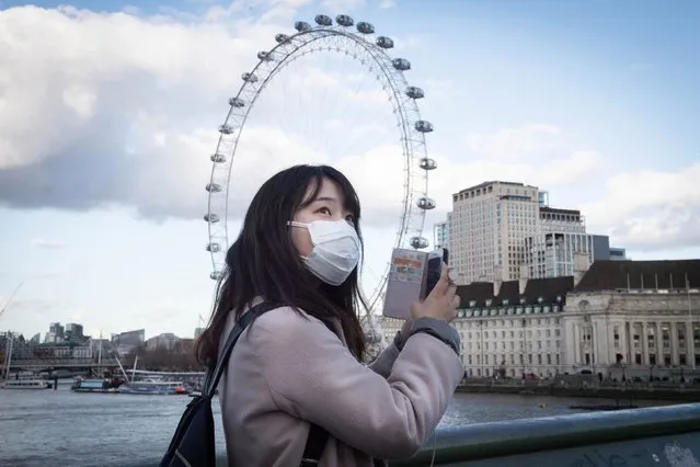 A woman wearing a face mask takes a photo on her phone from Westminster Bridge in London on March 2, 2020, as Shadow Health Secretary Jonathon Ashworth says he would support shutting down cities to control the spread of coronavirus. (Photo by Stefan Rousseau/PA Images via Getty Images)