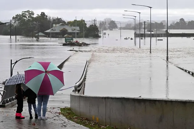 Residents look out toward flooded buildings next to the old Windsor Bridge along the overflowing Hawkesbury River in the northwestern Sydney suburb of Windsor on July 4, 2022. Rapidly rising rivers swamped swathes of rain-lashed Sydney on July 4, forcing thousands to flee “dangerous” floods as the city's largest dam spilled torrents of water. (Photo by Saeed Khan/AFP Photo)