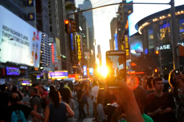 A man takes a photo with her phone as the sun sets over Manhattan aligned exactly with the streets in a phenomenon known as “Manhattanhenge”, in New York City, U.S., July 11, 2016. (Photo by Mark Kauzlarich/Reuters)