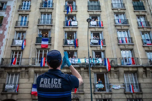 A police officer applauds for medical workers with people on a residential building in Saint-Mande, near Paris, France, on May 2, 2020. Giant masks are displayed on the balconies of a building in Saint-Mande with French flags in tribute to medical workers during a lockdown in France to stop the spread of COVID-19. (Photo by Chine Nouvelle/SIPA Press/Rex Features/Shutterstock)