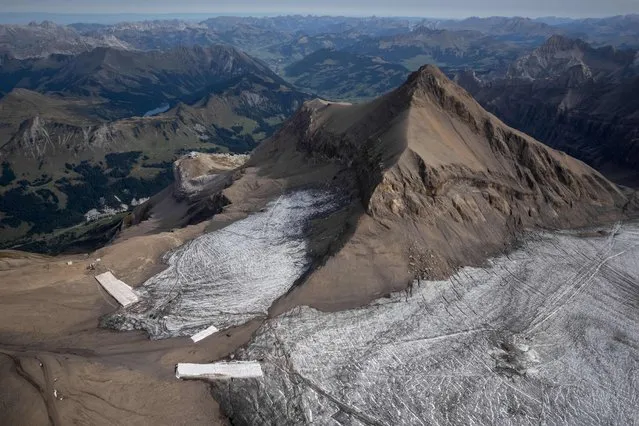 This aerial picture taken on September 13, 2022 at Glacier 3000 resort above Les Diablerets shows the Tsanfleuron pass free of the ice that covered it for at least 2,000 years next to blankets covering snow from the last winter season to prevent it from melting. The thick layer of ice that has covered a Swiss mountain pass between Scex Rouge glacier and Tsanfleuron glacier since at least the Roman era has melted away completely. Following a dry winter, the summer heatwaves hitting Europe have been catastrophic for the Alpine glaciers, which have been melting at an accelerated rate. (Photo by Fabrice Coffrini/AFP Photo)