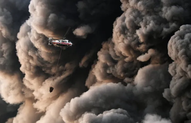A Russian emergency service helicopter carries water past billows of smoke as fire fighters battle the blaze in Sindika, a shopping mall selling construction materials, at MKAD Moscow Ring Road on the western outskirts of Moscow, Russia on October 8, 2017. (Photo by Maxim Grigoryev/TASS)
