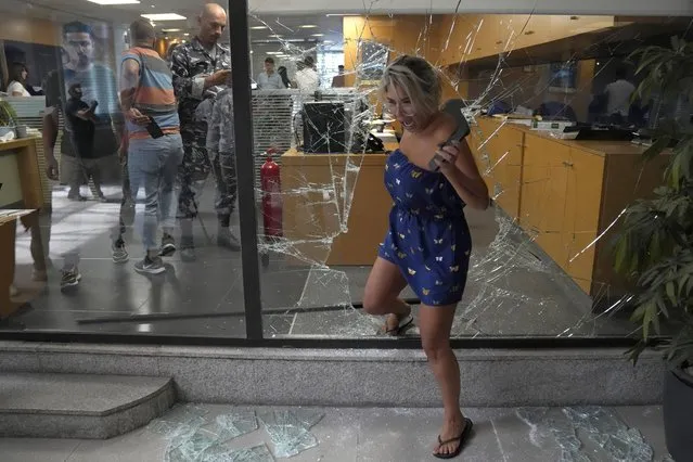 A bank employee exits the bank through a window broken by attackers, in Beirut, Lebanon, Wednesday, September 14, 2022. (Photo by Hussein Malla/AP Photo)