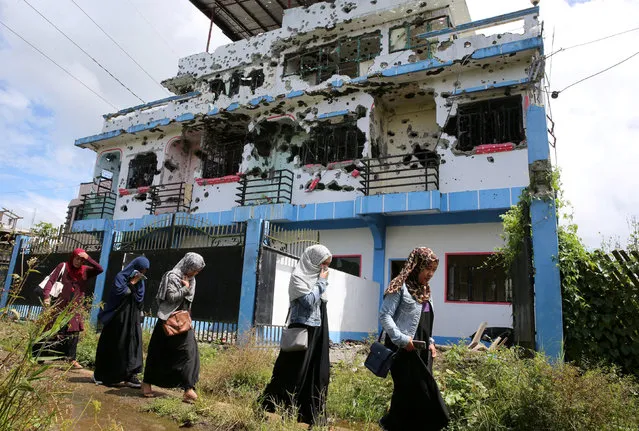 Residents who returned from evacuation centers walk past a bullet-ridden house believed to have been rented by pro-Islamic State militant group leaders Isnilon Hapilon and Omar Maute before their attack on the region, in Basak, Malutlut district in Marawi city, Philippines October 29, 2017. (Photo by Romeo Ranoco/Reuters)
