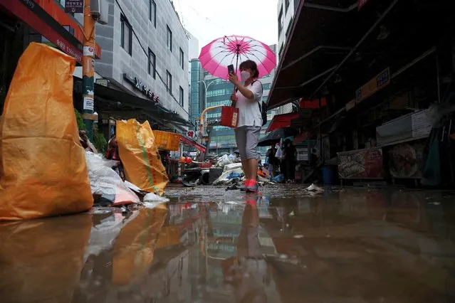 A woman using an umbrella takes photographs of a road that was flooded after torrential rain, at a traditional market in Seoul, South Korea on August 9, 2022. (Photo by Kim Hong-Ji/Reuters)