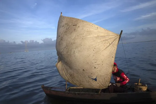 Yohandry Colina uses an oil-stained sheet for a sail on the boat he uses to put fish he catches in Lake Maracaibo in Cabimas, Venezuela, Wednesday, October 12, 2022. (Photo by Ariana Cubillos/AP Photo)