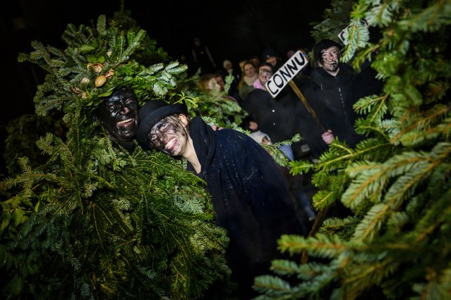 One of the village girls smiles with a man dressed with fir branches as they parade through the night during the “sortie des Sauvages” in the village of Le Noirmont, Switzerland, 25 January 2024 (issued 26 January 2024). The “sortie des Sauvages” (outing of the savages) traditionally marks the opening of the Franches-Montagnes carnival. During the event, men dressed as fir branches with blackened faces and carrying bells, lanterns or other whips, leave the farms to descend on the village to track down the 'baichatte' (the young women who dare defy the savages), who try to recognize the men hiding behind the costume. (Photo by Jean-Christophe Bott/EPA/EFE)